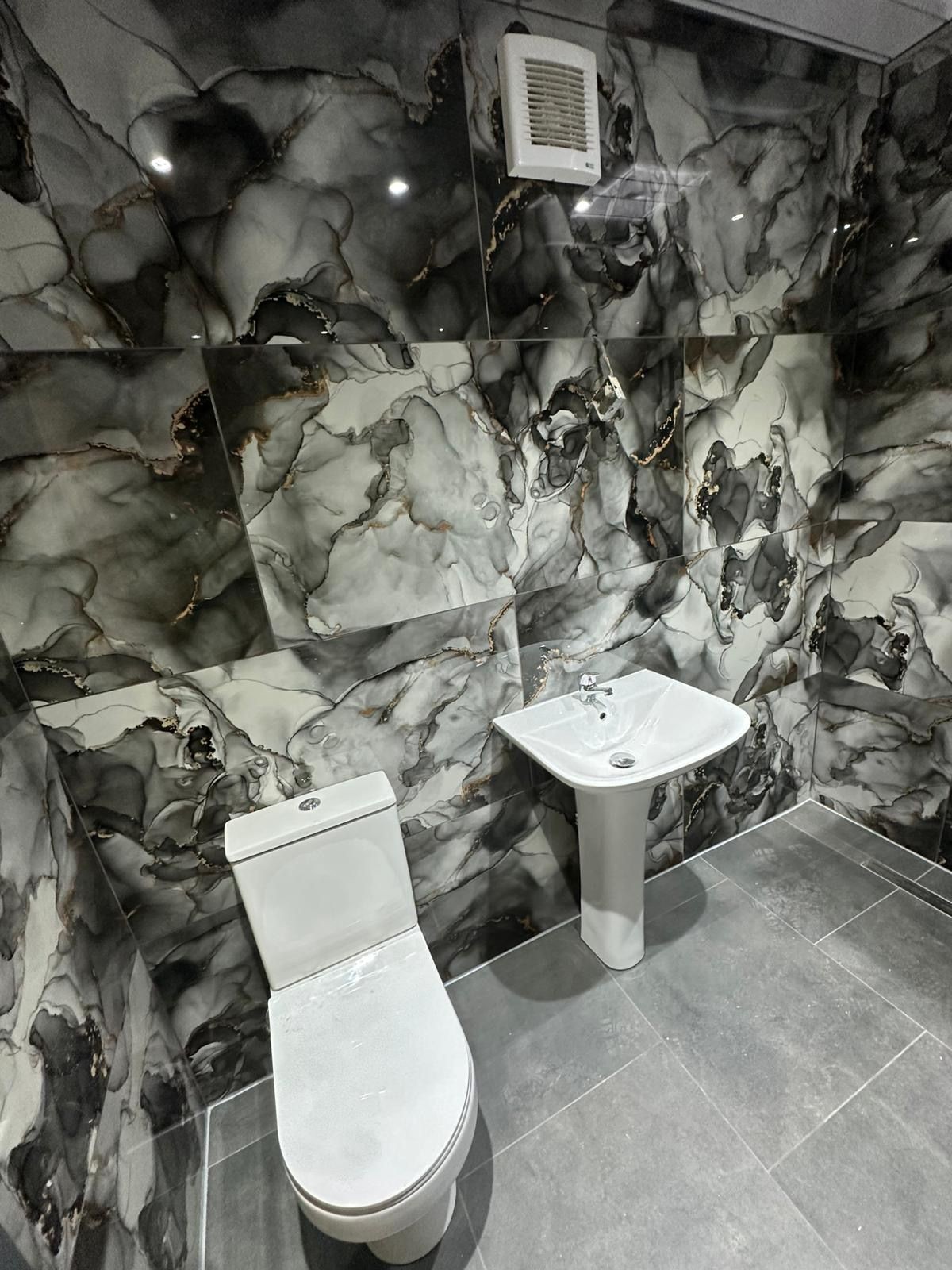 Modern bathroom with a white toilet, pedestal sink, and black marble tile walls.